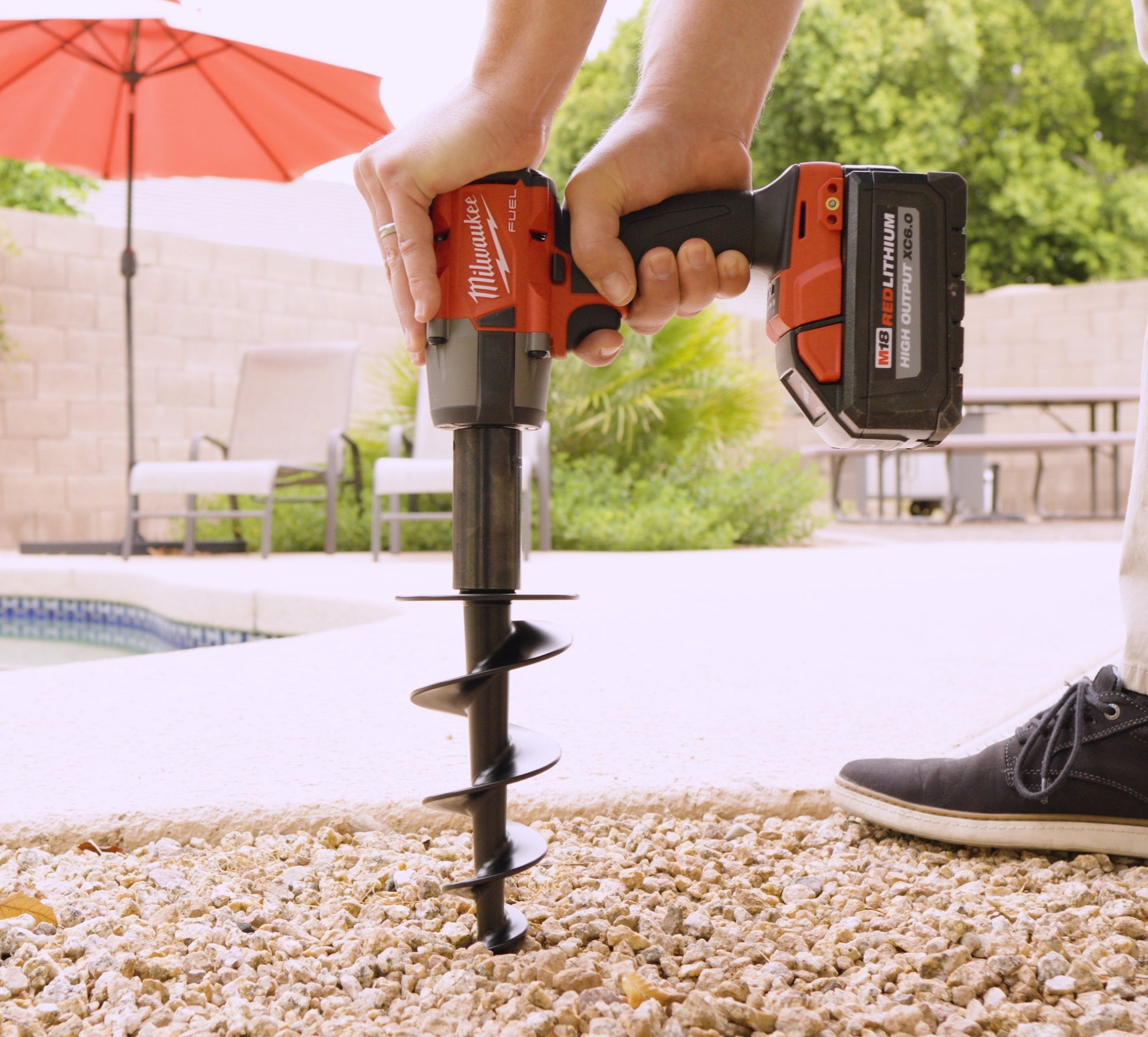 Person using a Milwaukee drill with a Soundstake on a patio with a pool and umbrella in the background.